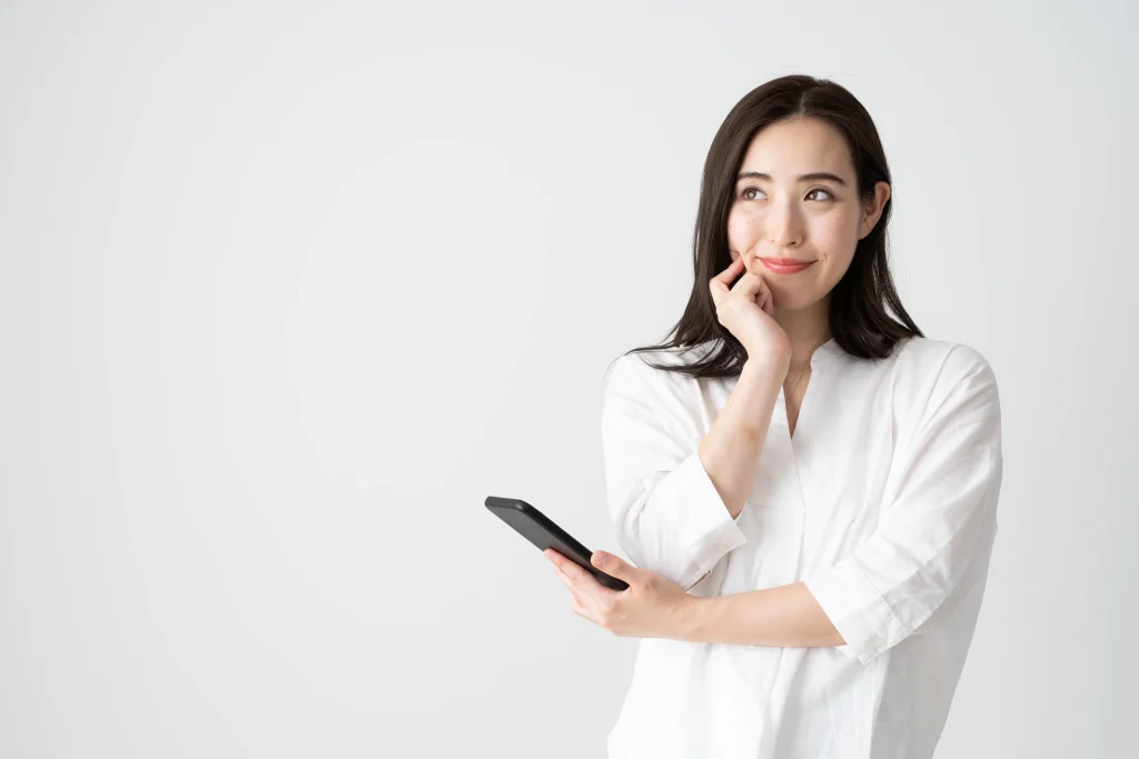 スマートフォンを片手に考えるジェスチャーをする女性