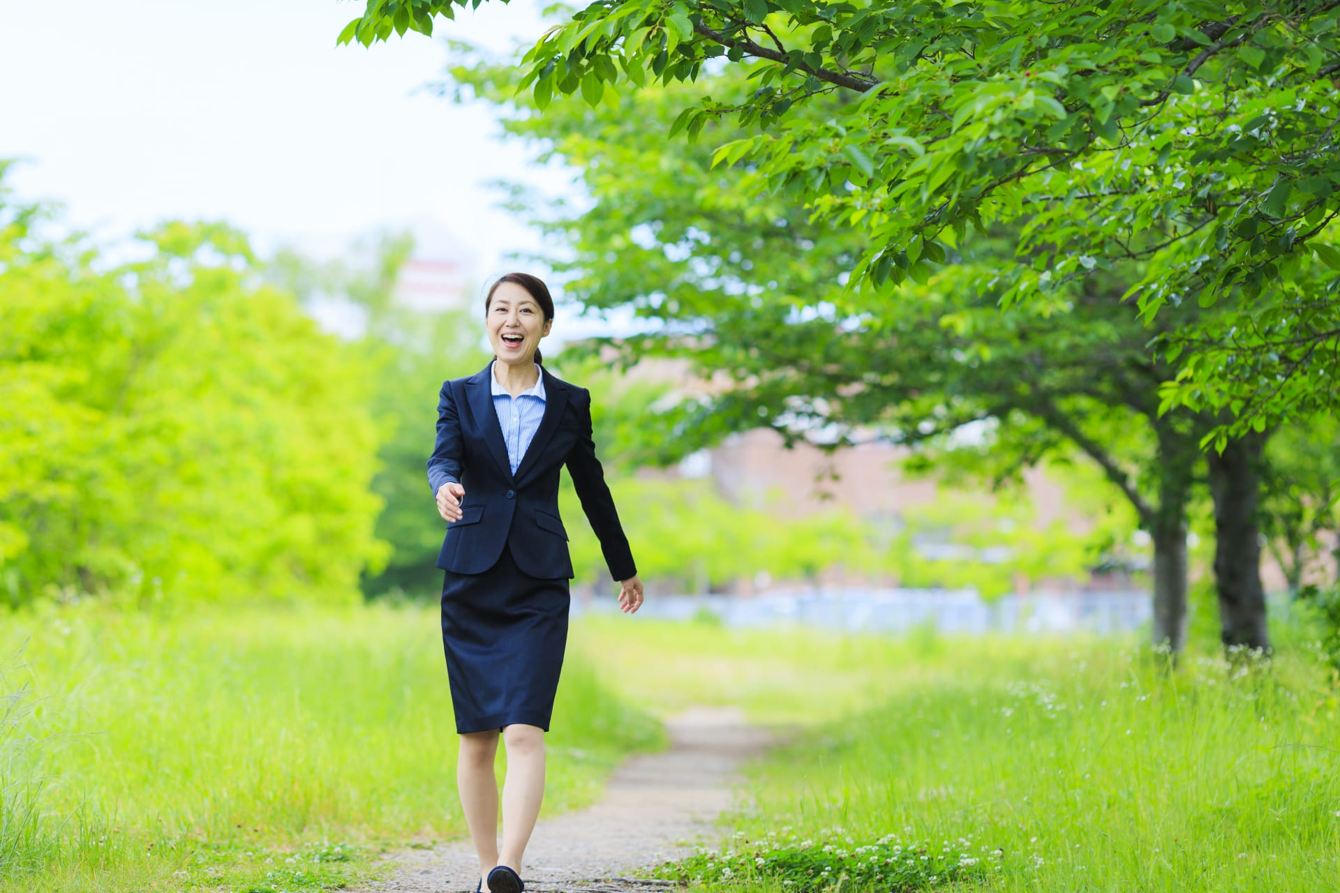 緑が鮮やかな小道を歩くスーツを着た女性