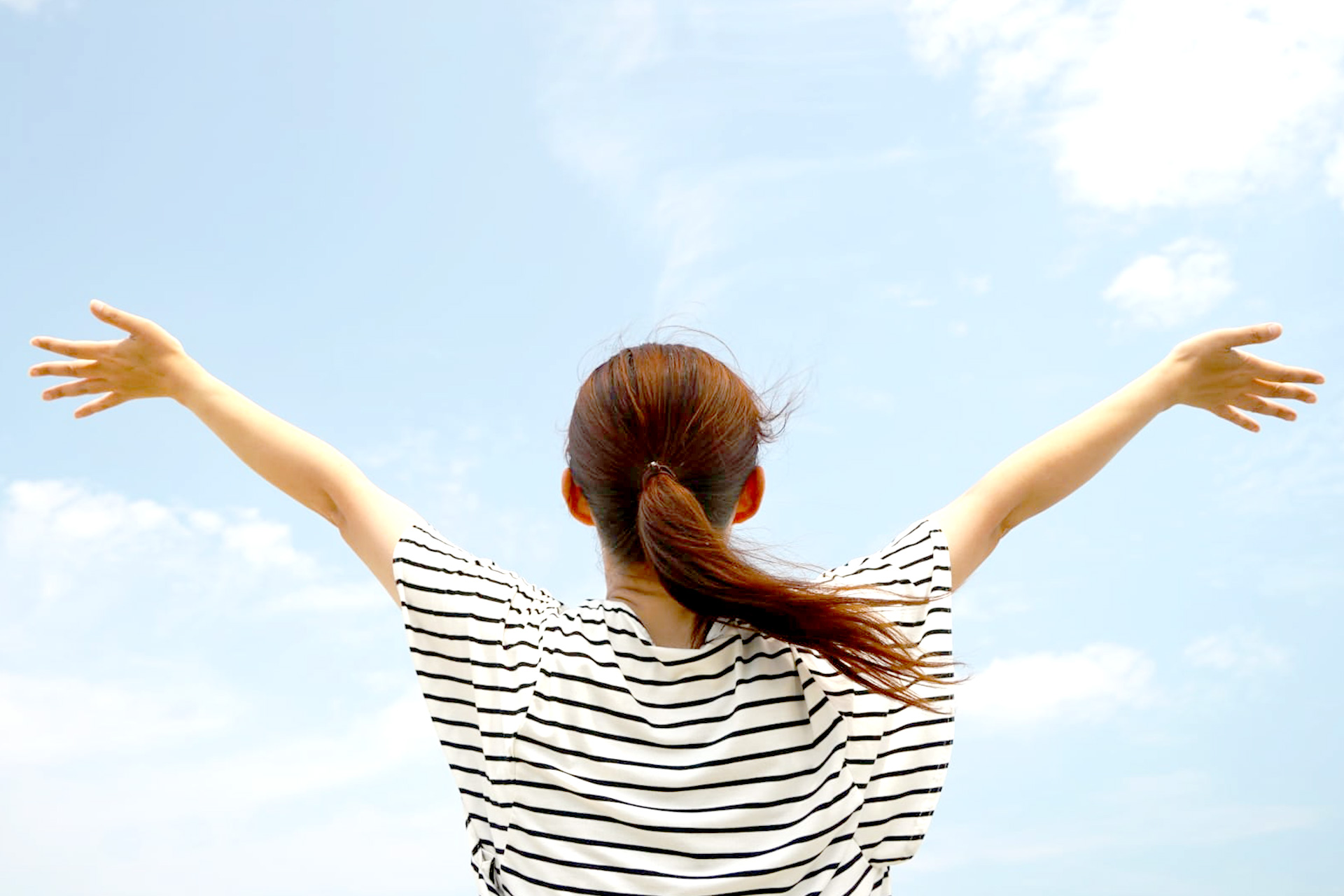 空に向かって手を広げる女性の後姿