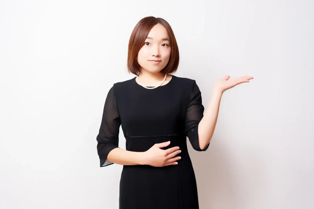 案内のポーズをしている喪服を着ている女性