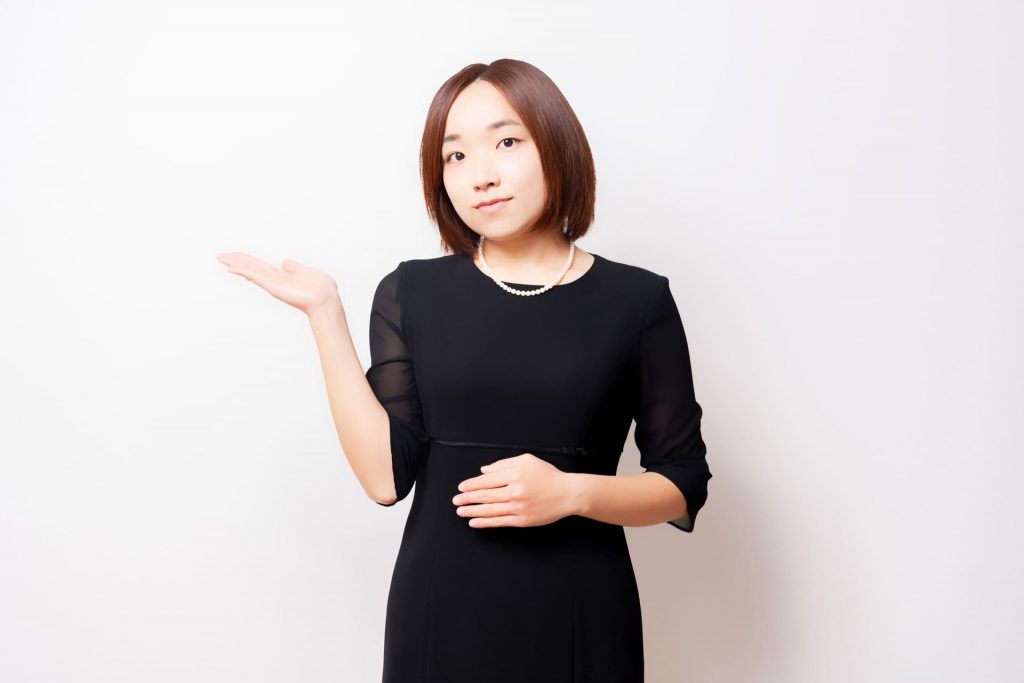 案内のポーズをする喪服を着た女性